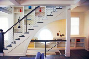 Modern custom cable rail staircase system with custom cabinetry and a nautically-inspired window behind